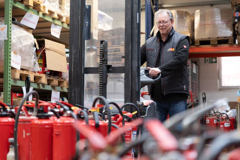 Mitarbeiter transportiert Feuerloescher auf Hubwagen